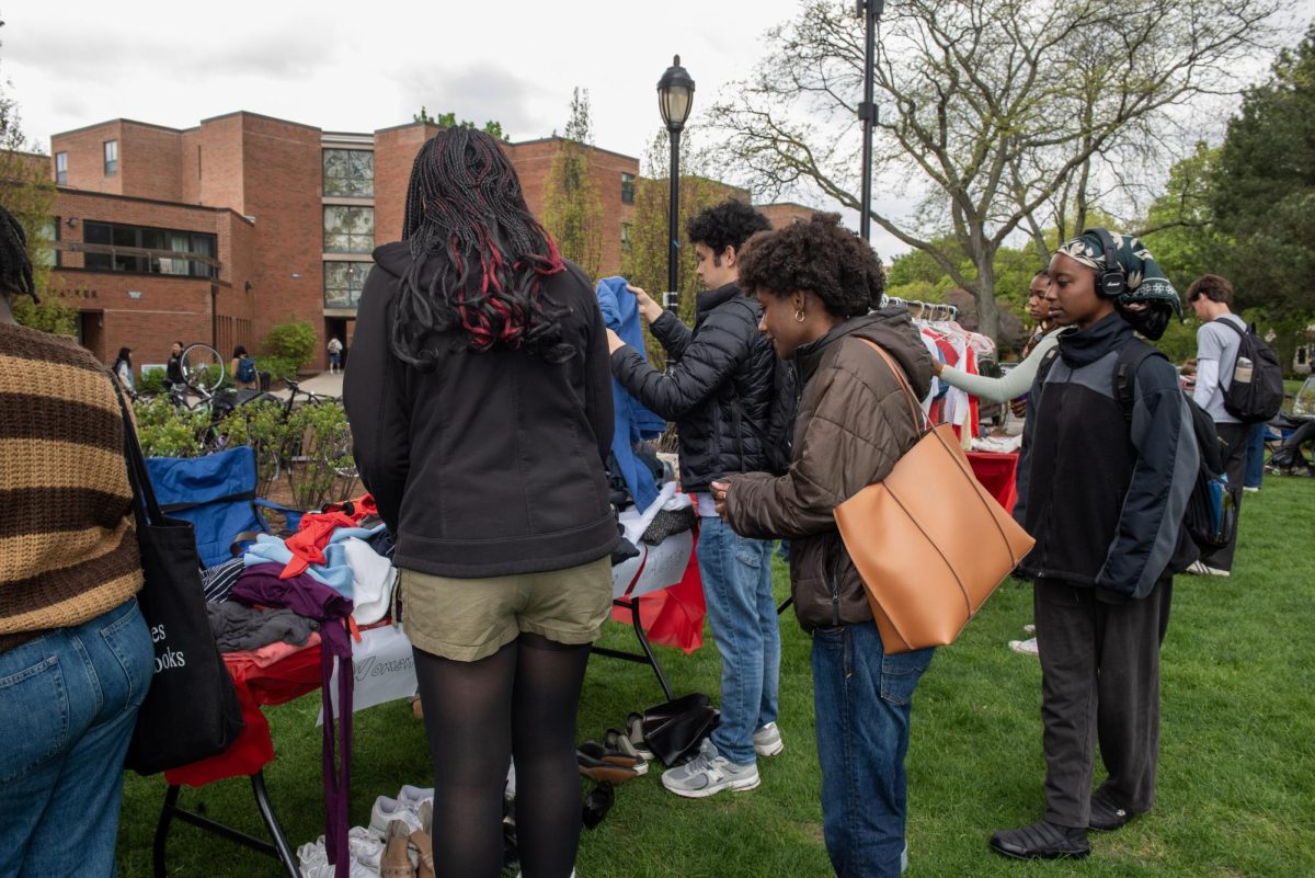 People look through clothes covering a table outside.