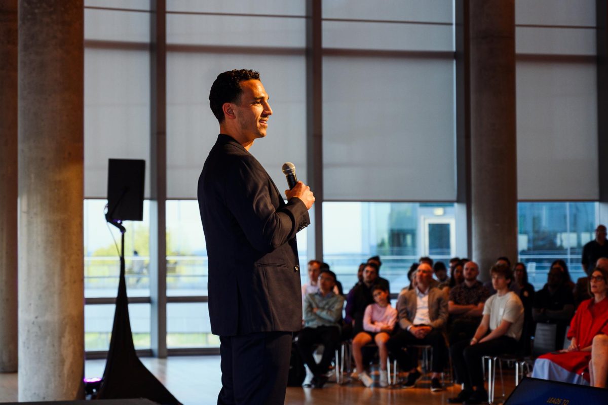 A person with a microphone speaks facing an audience.