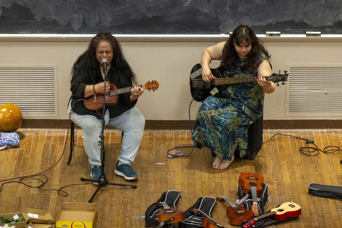 One performer sings into a microphone and plays ukulele as another performer plays guitar.