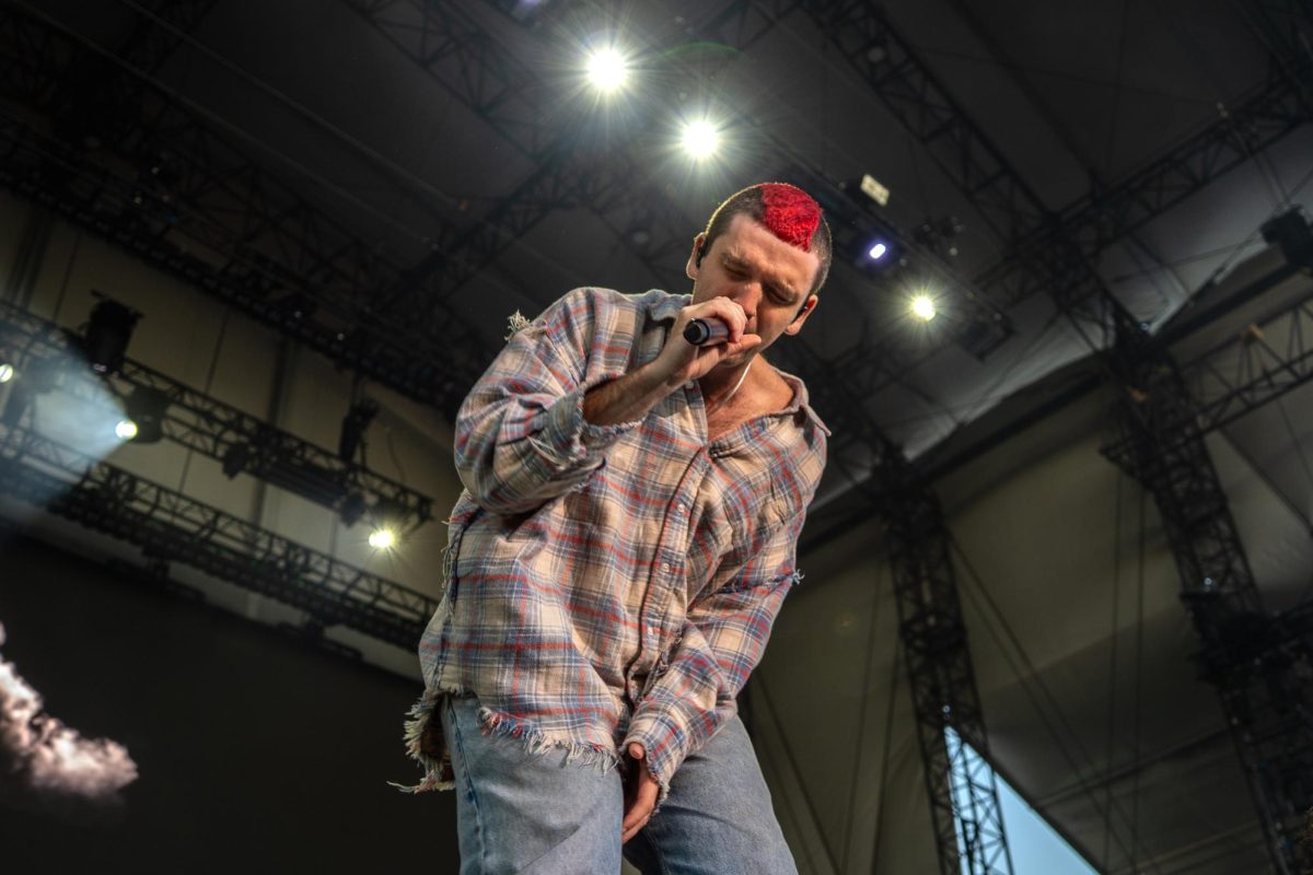 A man sings into a microphone with his hand on his chest.