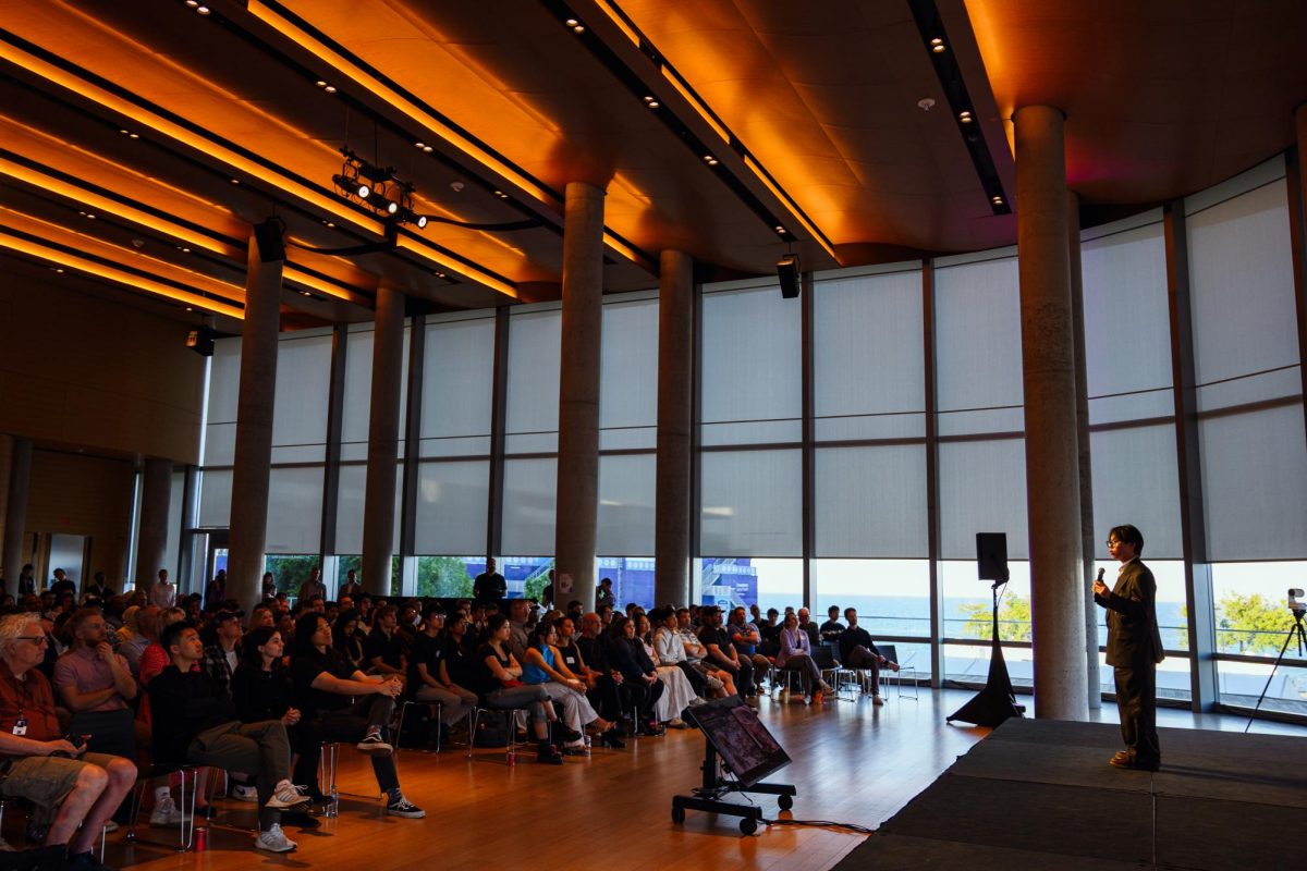 A person in a suit speaks to the audience from a stage.