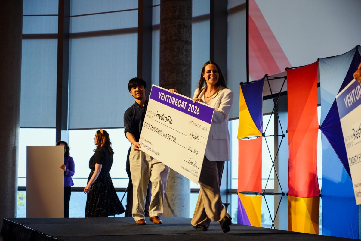 Two people walk across the stage holding a large check.