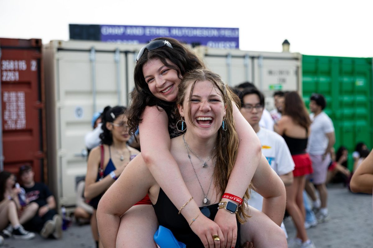 An attendee gives their friend a piggyback ride. Both are smiling broadly at the camera.