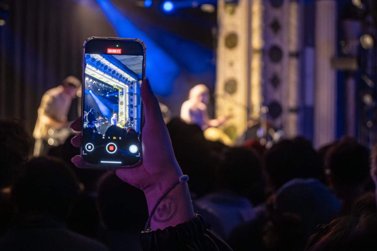 An attendee holds up their phone to record the performance. The performer is visible in the background.