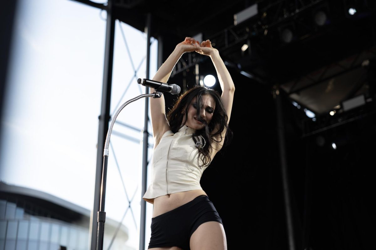A performer holds their hands above their head and sways.