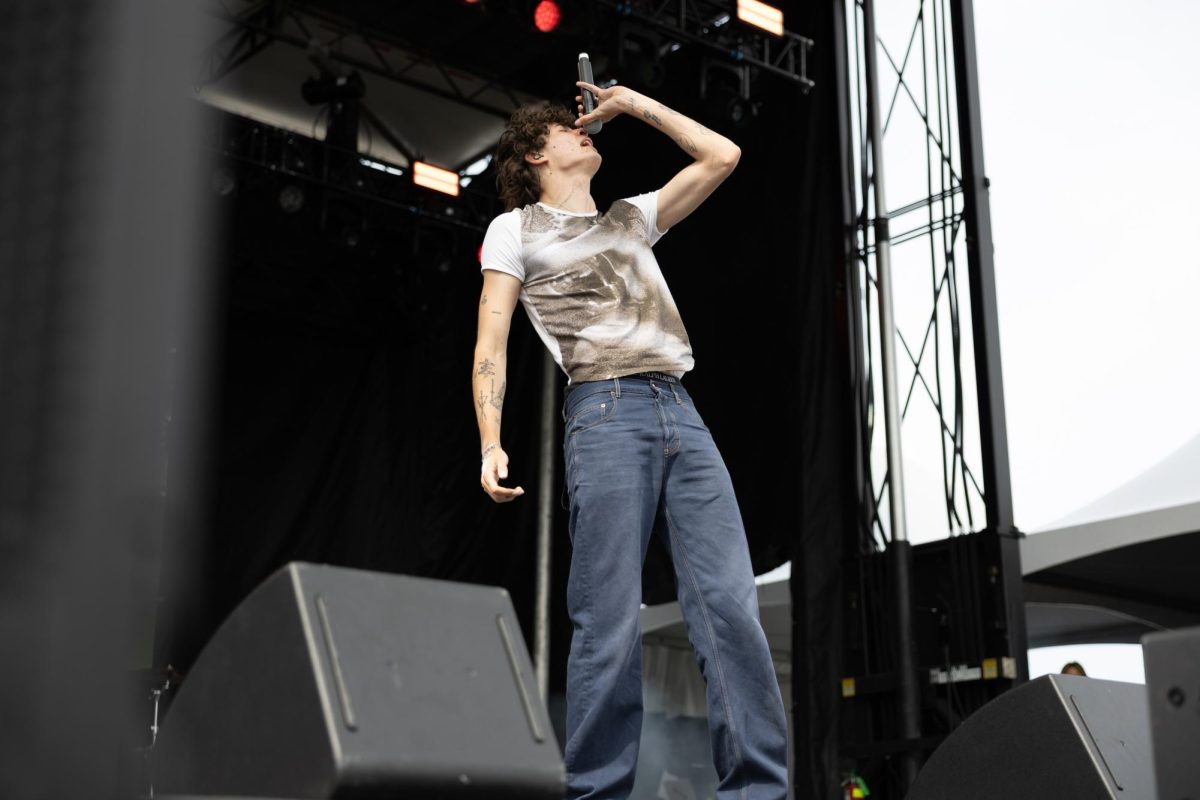 A person wearing a white t-shirt tilts their head up and holds a microphone above their head.
