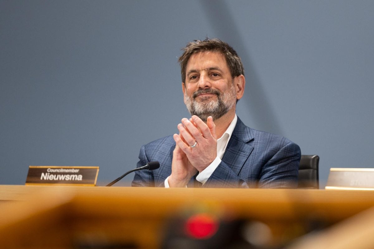 Alderman Jonathan Nieuwsma smiles and claps behind a desk with a mic on it.