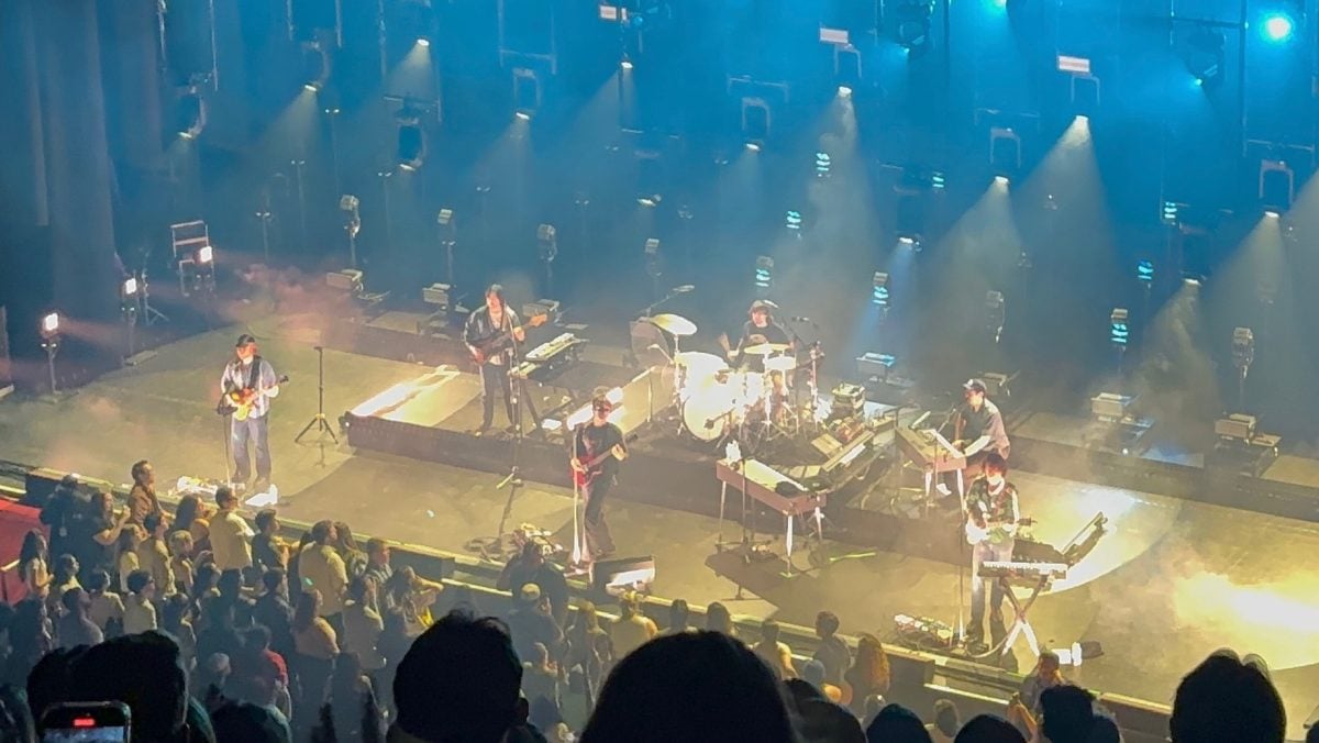 A person plays a guitar with a band behind him.