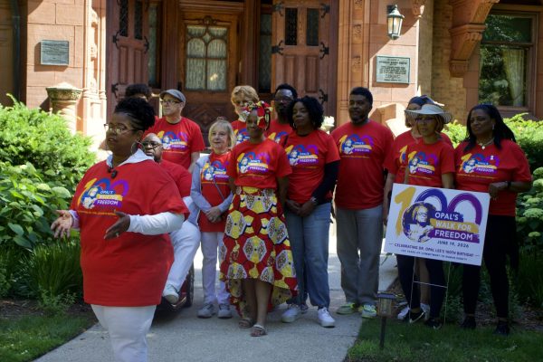 People stand in front of a building as one person speaks.