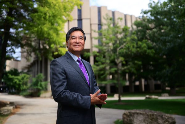 A person stands in front of trees and a building.