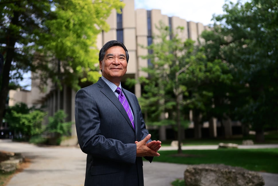 A person stands in front of trees and a building.