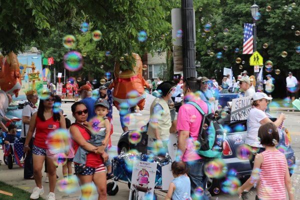 People mingle during a parade with bubbles floating in the foreground