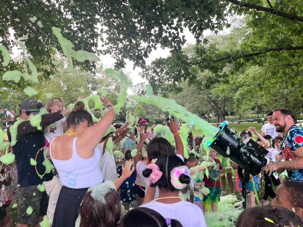 Green foam is shot out from a cannon onto a group of people.