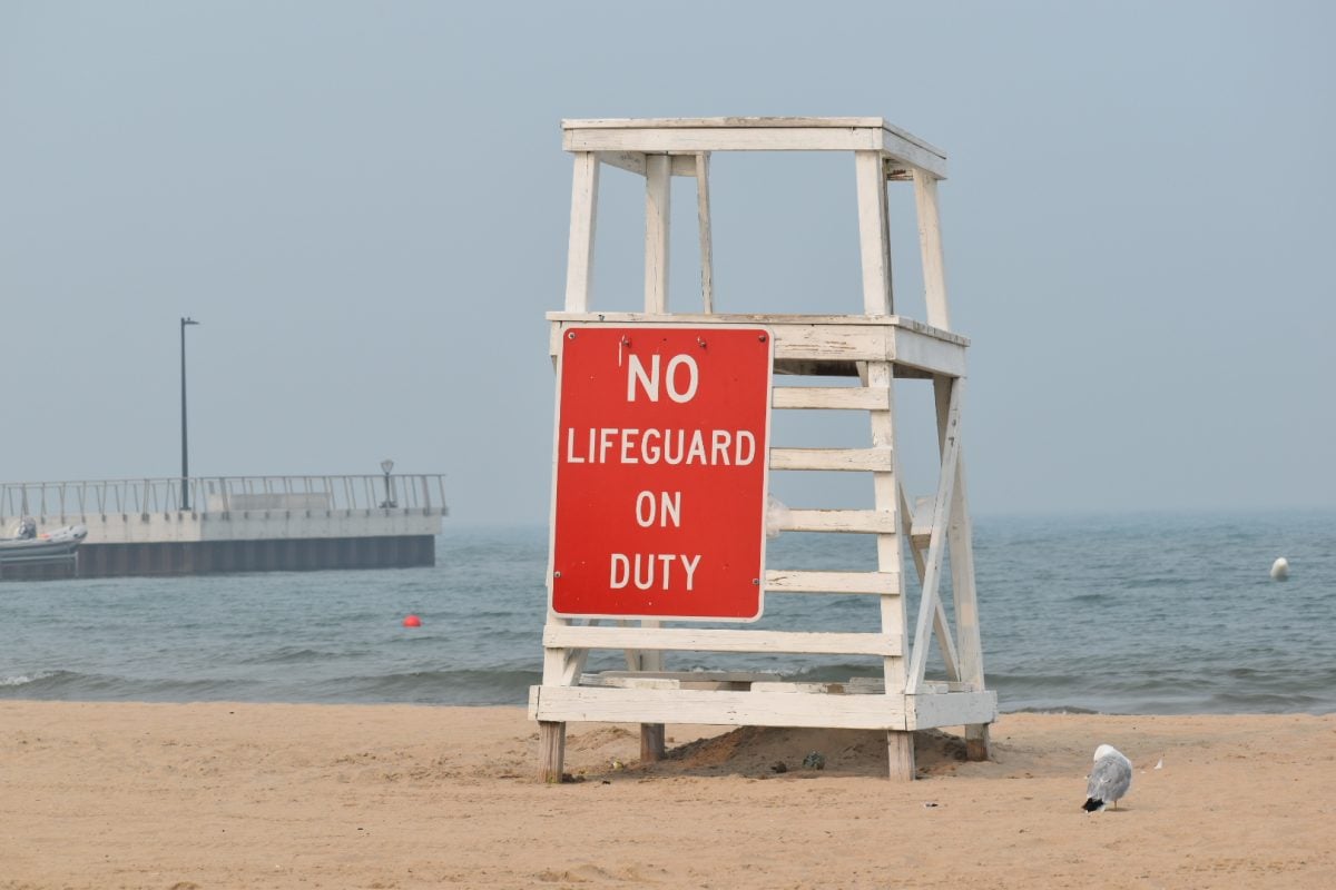 A photo of a sign that reads “No lifeguard on duty” hanging from a high chair.