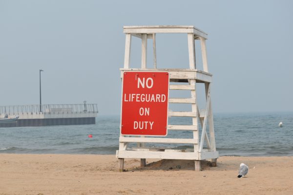 A photo of a sign that reads “No lifeguard on duty” hanging from a high chair.