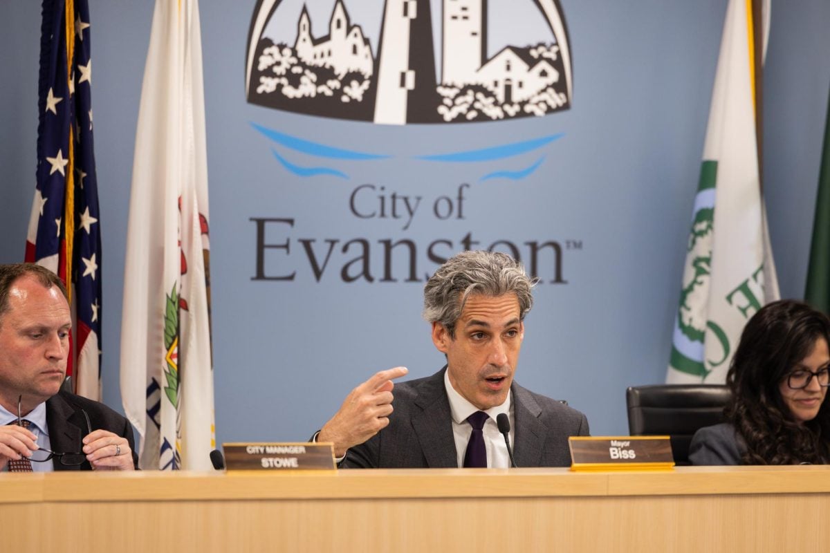 People sit behind a dais in front of a “City of Evanston” logo on the wall.