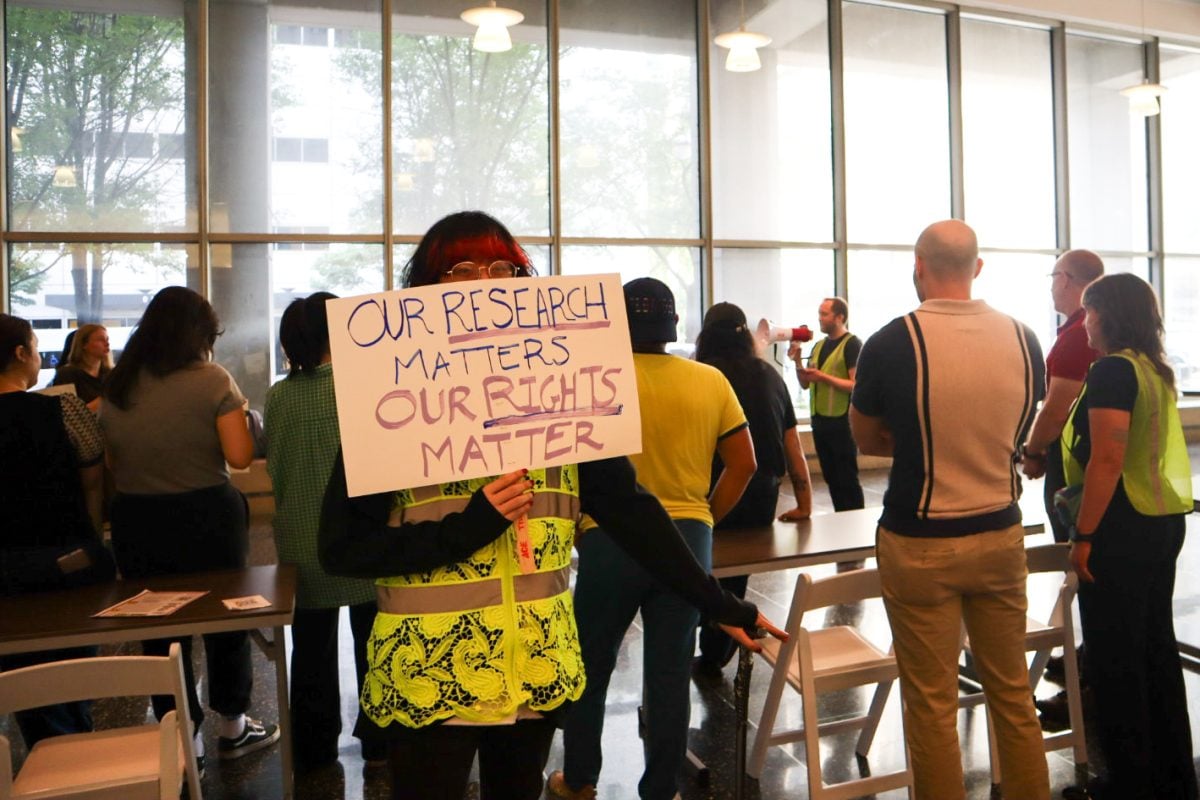 A person holds a sign that reads “OUR RESEARCH MATTERS, OUR RIGHTS MATTER.”