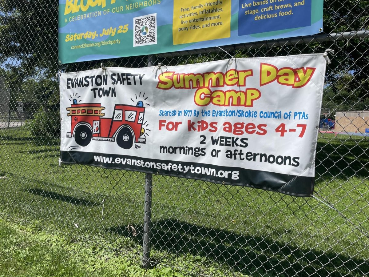 A white banner advertising a summer camp hangs on a chain-link fence.