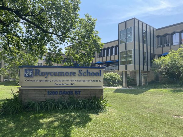 A tan school building next to a sign with blue lettering that reads “Roycemore School.”