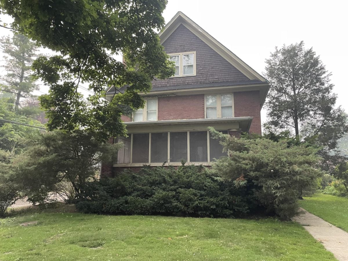 A brown house with a green backyard stands in front of a cloudy sky.