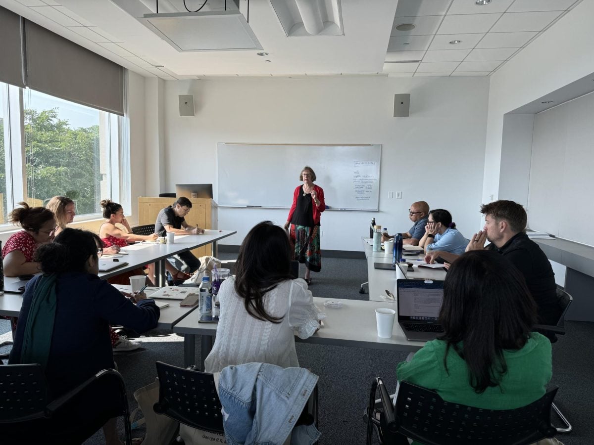 People seated around three tables in a classroom with an instructor in the middle.