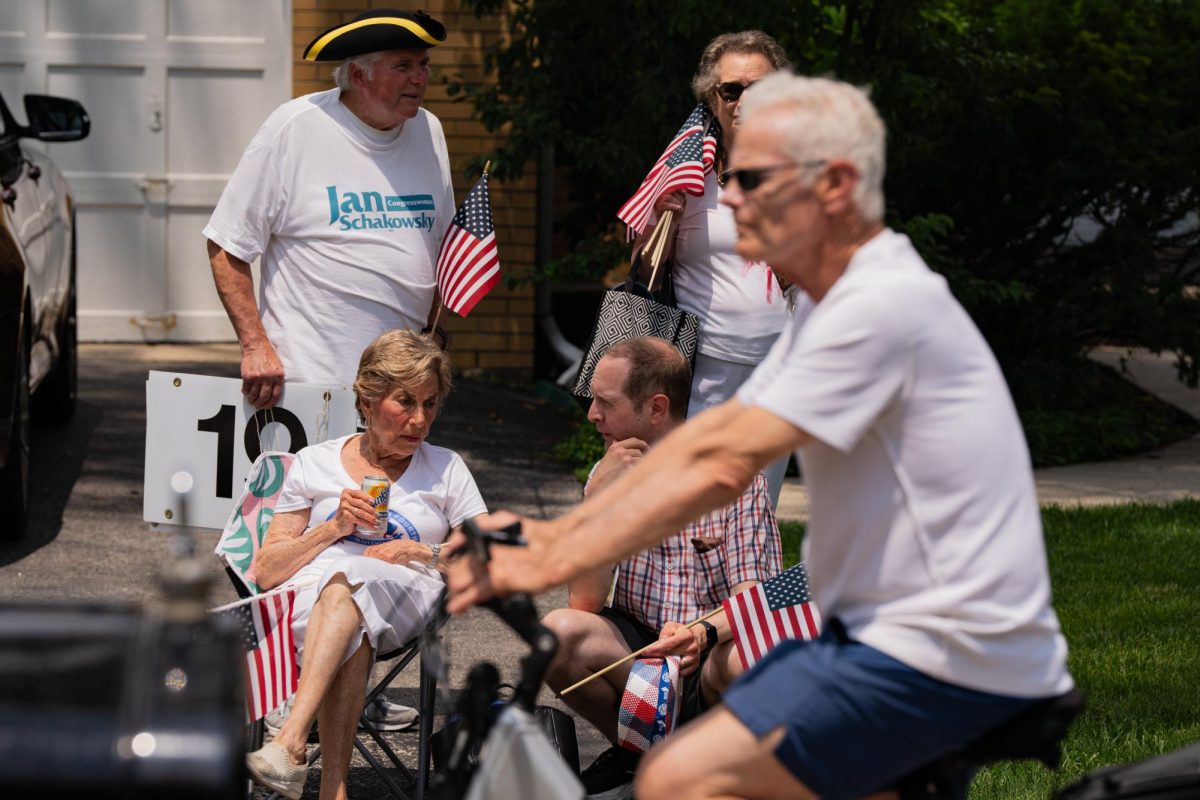 A blurry biker rides past four people watching the parade