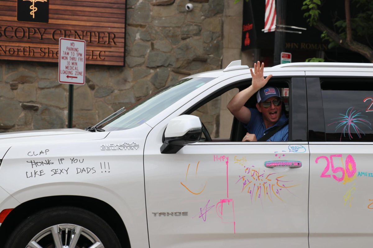 A person waves from the window of a car covered in writing, including the sentence, “Clap if you like sexy dads!”