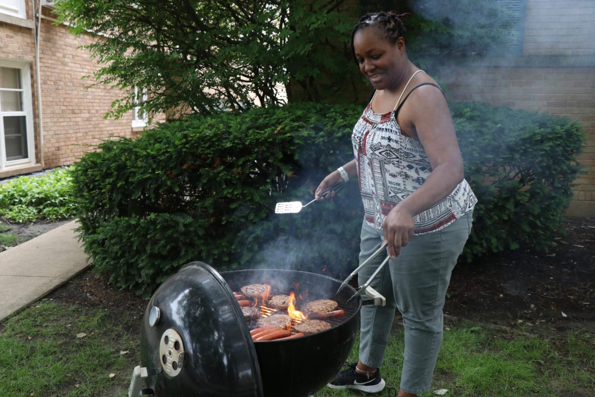 A person smiles while grilling hamburgers and hotdogs