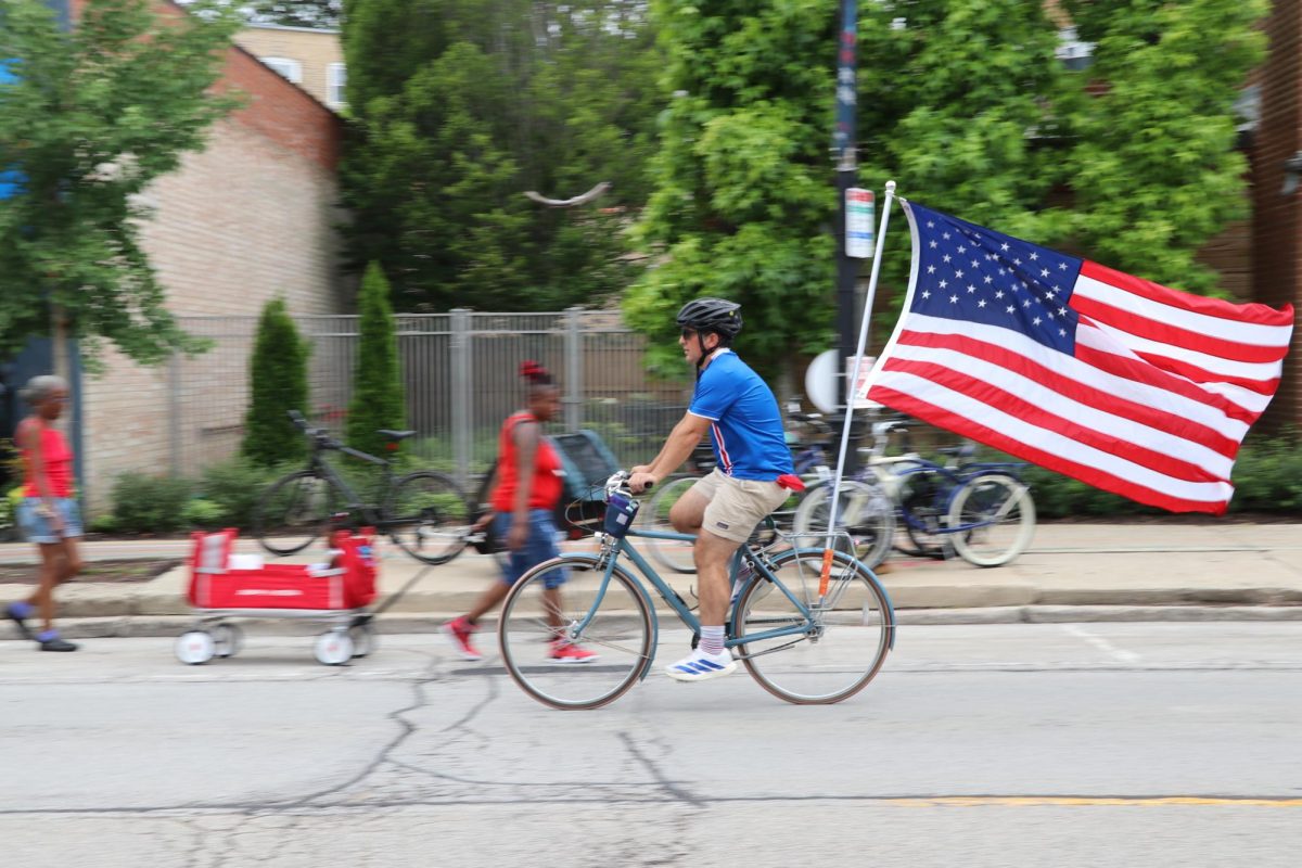 A biker pedals past attendees, an American flag waving from the back of their bike