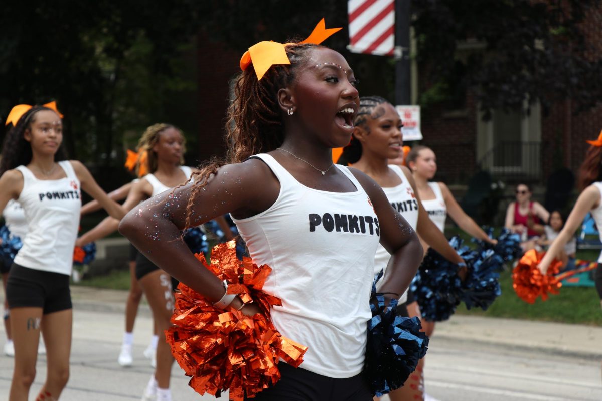 A person holding orange and blue pompoms performs with their dance troupe