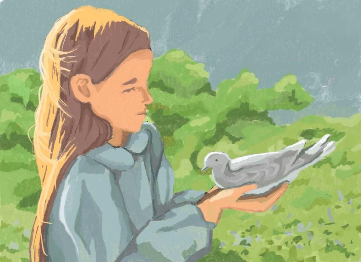 A girl holds a bird in her hand outside on the grass.