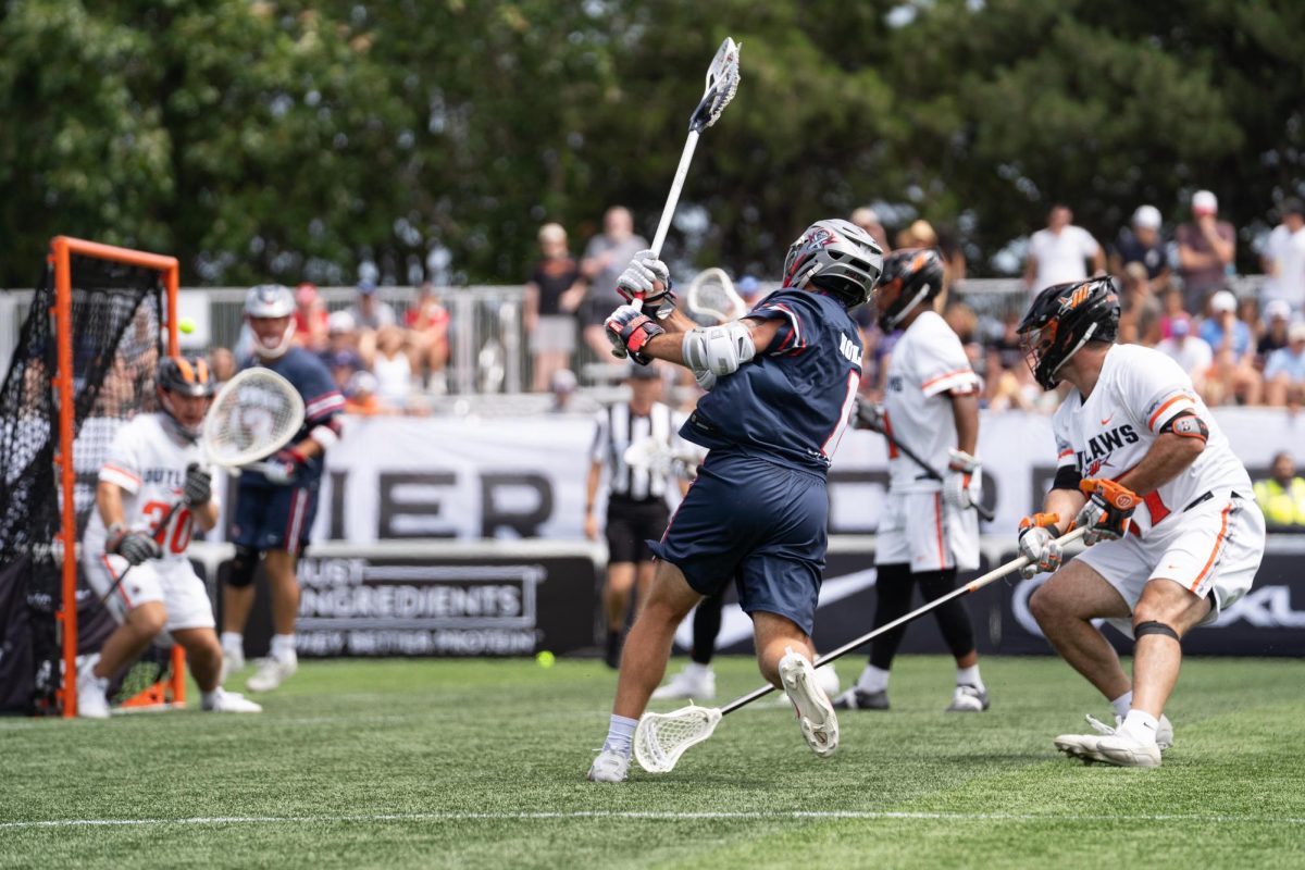 A player in a dark blue jersey shoots while defended.